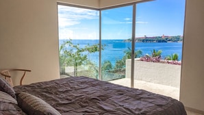 Een slaapkamer met een groot bed, uitzicht op zee en een balkon met planten.
