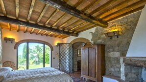 A bedroom with a large bed, a stone fireplace, and a view of the outdoors. - Beautiful private villa with private pool, WIFI, A/C, TV and balcony, close to Florence (Pontassieve)