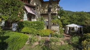 A traditional house with a balcony, surrounded by lush greenery and a tent set up nearby.
