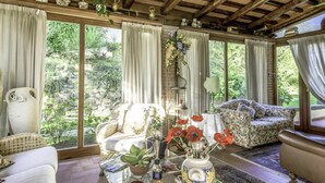 A cozy room with a wooden ceiling, large windows, a sofa, a chair, and a table with a vase of flowers.