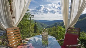 A glass table with chairs, a view of a mountainous landscape, and white curtains.