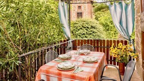 A covered outdoor dining area with a table set for two, surrounded by lush greenery and a rustic stone building in the background. - Cosy apartment in villa for 4 guests with A/C, WIFI, pool, TV and patio (Città Della Pieve)