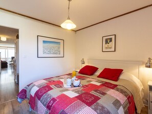 A bedroom with a large bed, red pillows, a quilt, and a nightstand with a lamp. There are two framed pictures on the wall.