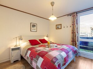 Un dormitorio con una cama grande, dos mesitas de noche, una ventana con cortinas y vistas a un edificio.