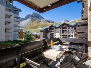 A wooden outdoor seating area with a table and benches, overlooking a mountain range and buildings with wooden facades.
