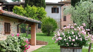 Un jardin agrémenté d’un bâtiment en pierre, d’un bac à fleurs en bois contenant des fleurs roses et d’un chemin pavé de briques.