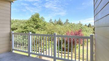 A covered porch with a white fence, a concrete floor, and a view of trees and shrubs.