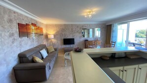 Ein modernes Wohnzimmer mit Sofa, Essbereich mit Tisch, Fernseher und Kücheninsel.