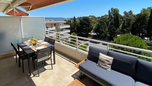 Ein Balkon mit Esstisch, einer Couch und Blick auf das Meer und die Gebäude.