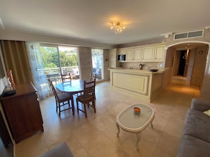 Amplia sala de estar con mesa de comedor, sofá, pequeña mesa de centro y cocina con armarios blancos y una isla central.