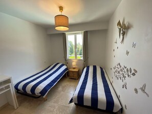 A room with two beds, a window, a lamp, and wall decorations.