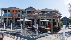 An outdoor seating area with tables and chairs, a covered patio, and a building with a sign reading "The Grill" in the background.