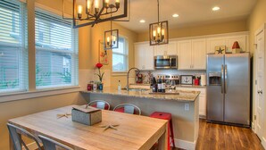 A modern kitchen with white cabinets, stainless steel appliances, and a wooden dining table.