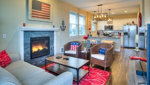 A spacious living room with a fireplace, comfortable seating, and a kitchen in the background.