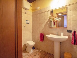 Een badkamer met toilet, wastafel en spiegel. Er hangt een bord aan de muur en een handdoekrek met handdoeken.
