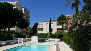 Une piscine à l’eau d’un bleu limpide, entourée d’une clôture et jouxtant un bâtiment doté de balcons.
