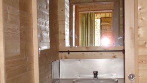 Een kleine badkamer met een houten inrichting, een witte wastafel, een spiegel en een raam met een groene gordijn.