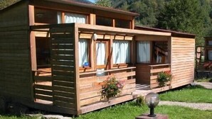Een houten hutje met een veranda, ramen met gordijnen en een kleine tuin.