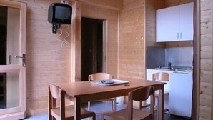 Een houten blokhut van binnen, met een eettafel, stoelen, een televisie en een keuken.
