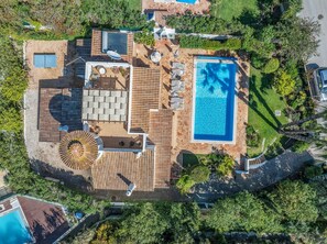 An aerial view of a property with a swimming pool, outdoor seating area, and a patio with a sun umbrella.