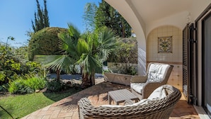Eine Terrasse im Freien mit Korbmöbeln, einer Palme und einer gefliesten Wand.