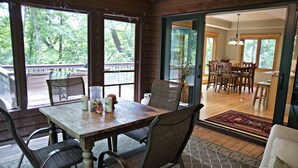A wooden dining table with chairs, a potted plant, and a window with a view of trees.