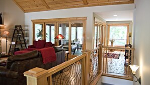 A spacious living area with a wooden ceiling, a red sofa, a dining table, and a staircase with a railing.