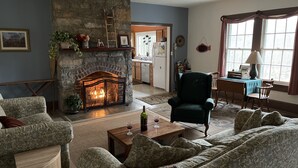 A cozy living room with a stone fireplace, a dining area, and a kitchen in the background.