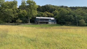A rustic blue barn with a porch, surrounded by a field and dense forest.