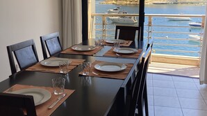 Une table à manger dressée pour quatre personnes, avec vue sur la mer et un bâtiment historique en arrière-plan.