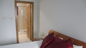 Une chambre d’hôtel avec un lit, une table de chevet, une lampe et une porte en bois donnant sur une salle de bain.