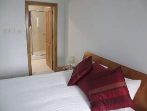 Una habitación de hotel con una cama, una mesita de noche, una lámpara y una puerta de madera que da al baño.