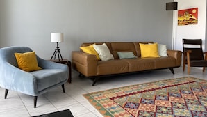 Un salon avec un canapé marron, un fauteuil bleu, un tapis à motifs et une lampe.