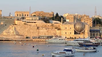 Uma marina com barcos atracados, um edifício grande com estrutura em cúpula e um morro com construções.