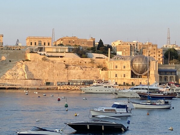Un puerto deportivo con barcos amarrados, un edificio grande con una estructura en forma de cúpula y una colina con edificios.