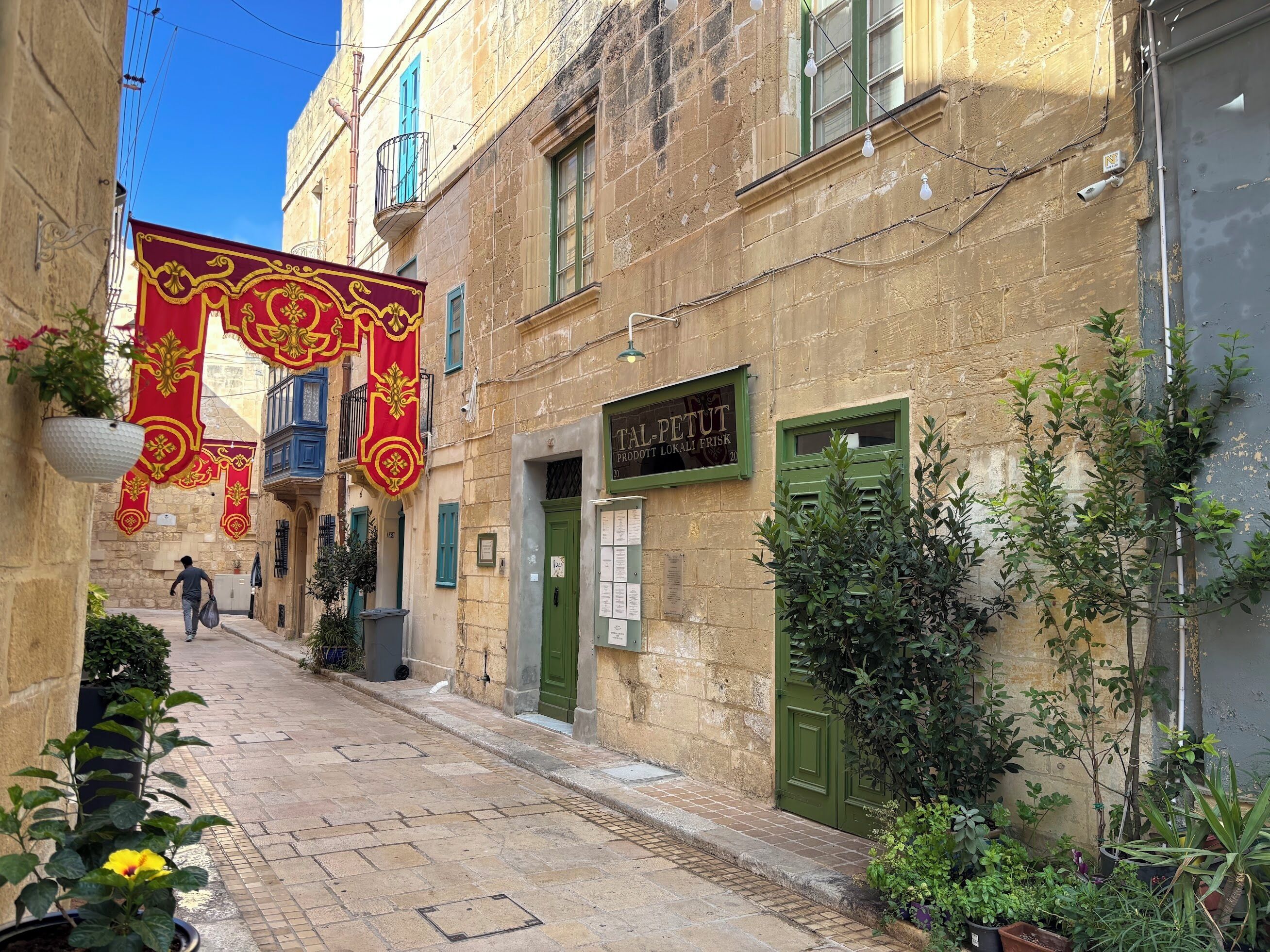 A narrow street with a building featuring a green door and a sign reading 'TAL-PETUT'.