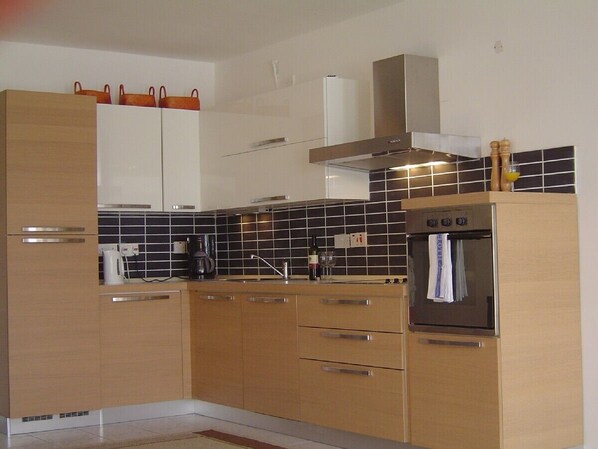 Una cocina moderna con armarios de madera, horno integrado y salpicadero con azulejos negros.