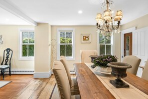 Enjoy meals in this dining area with a table for four, a chandelier, and a view of lush greenery.