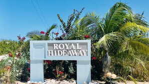 Schild mit der Aufschrift "ROYAL HIDEAWAY" vor einer tropischen Pflanzenkulisse und blauem Himmel.