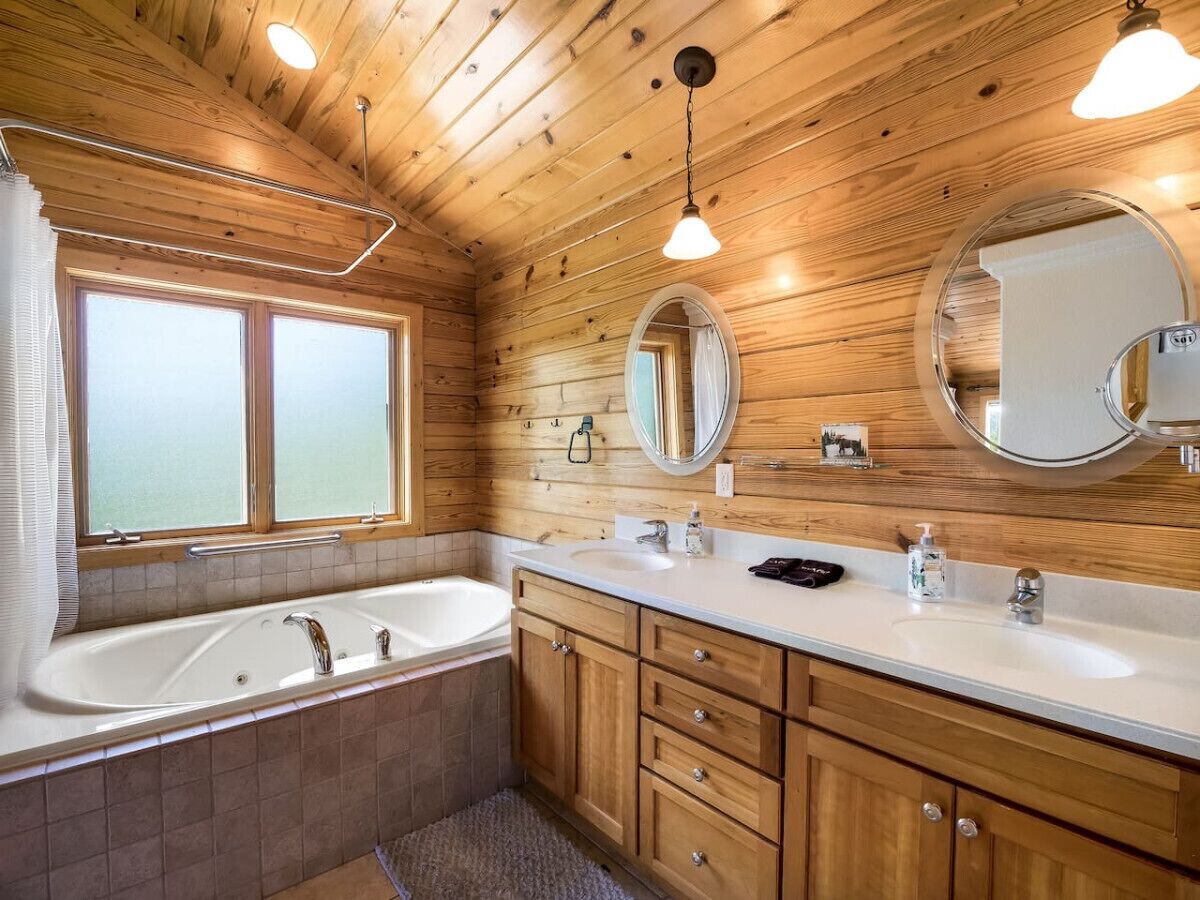 Un baño con paneles de madera, una bañera, dos lavamanos y armarios de madera.