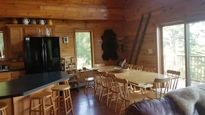 Een houten chalet van binnen met een keuken, eethoek en grote ramen.