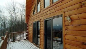 Een houten chalet met een balkon, grote schuiframen en uitzicht op een besneeuwd landschap.