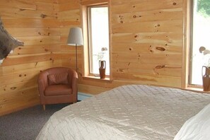 Une pièce de cabane en bois comprenant un lit, une chaise et une fenêtre agrémentée d’un vase.