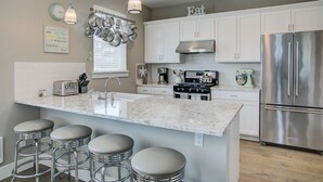 Een moderne keuken met een centraal eiland, roestvrijstalen apparatuur en barstoelen.