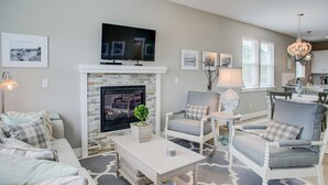 Een woonkamer met een open haard, een televisie en een eethoek op de achtergrond.