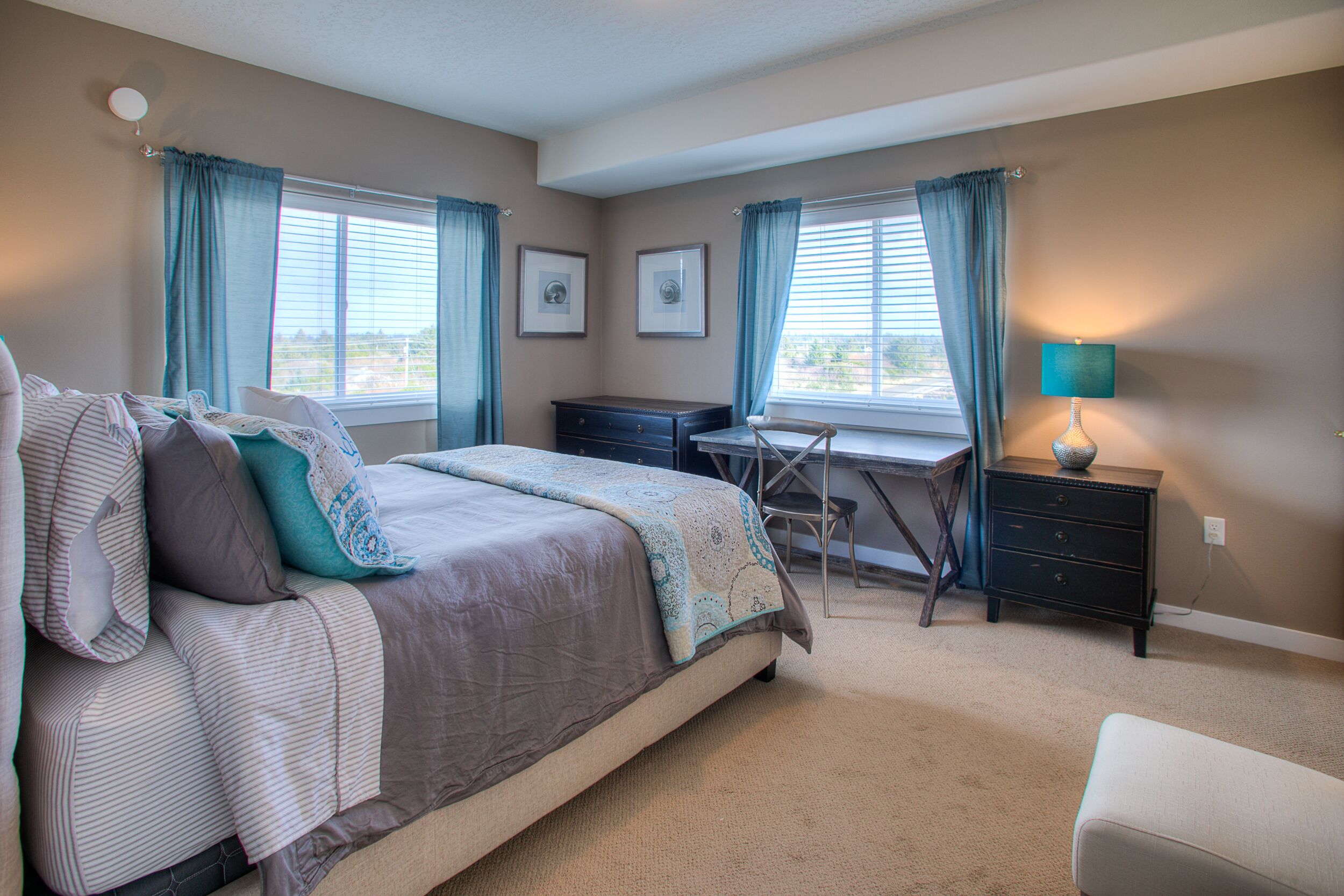Una camera da letto con un letto, una scrivania, una sedia, una cassettiera e una lampada.