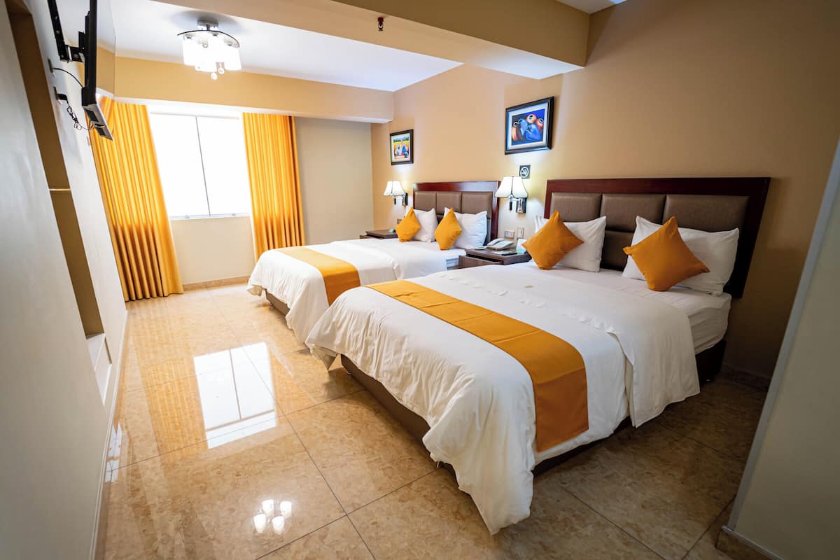 A hotel room with two beds, a large window with yellow curtains, and a ceiling fan.