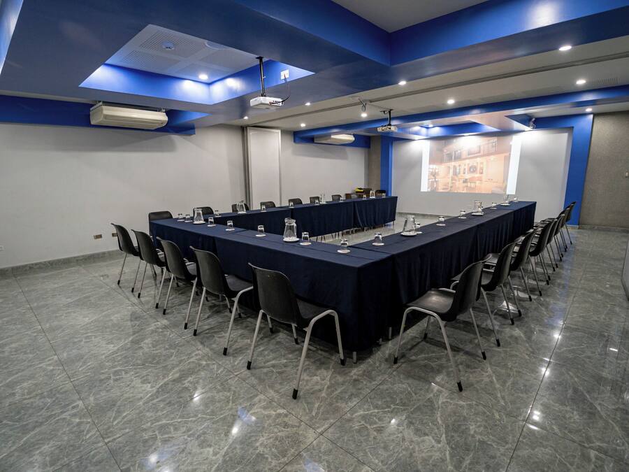 Un salón de conferencias con una larga mesa, sillas y una pantalla para proyector.