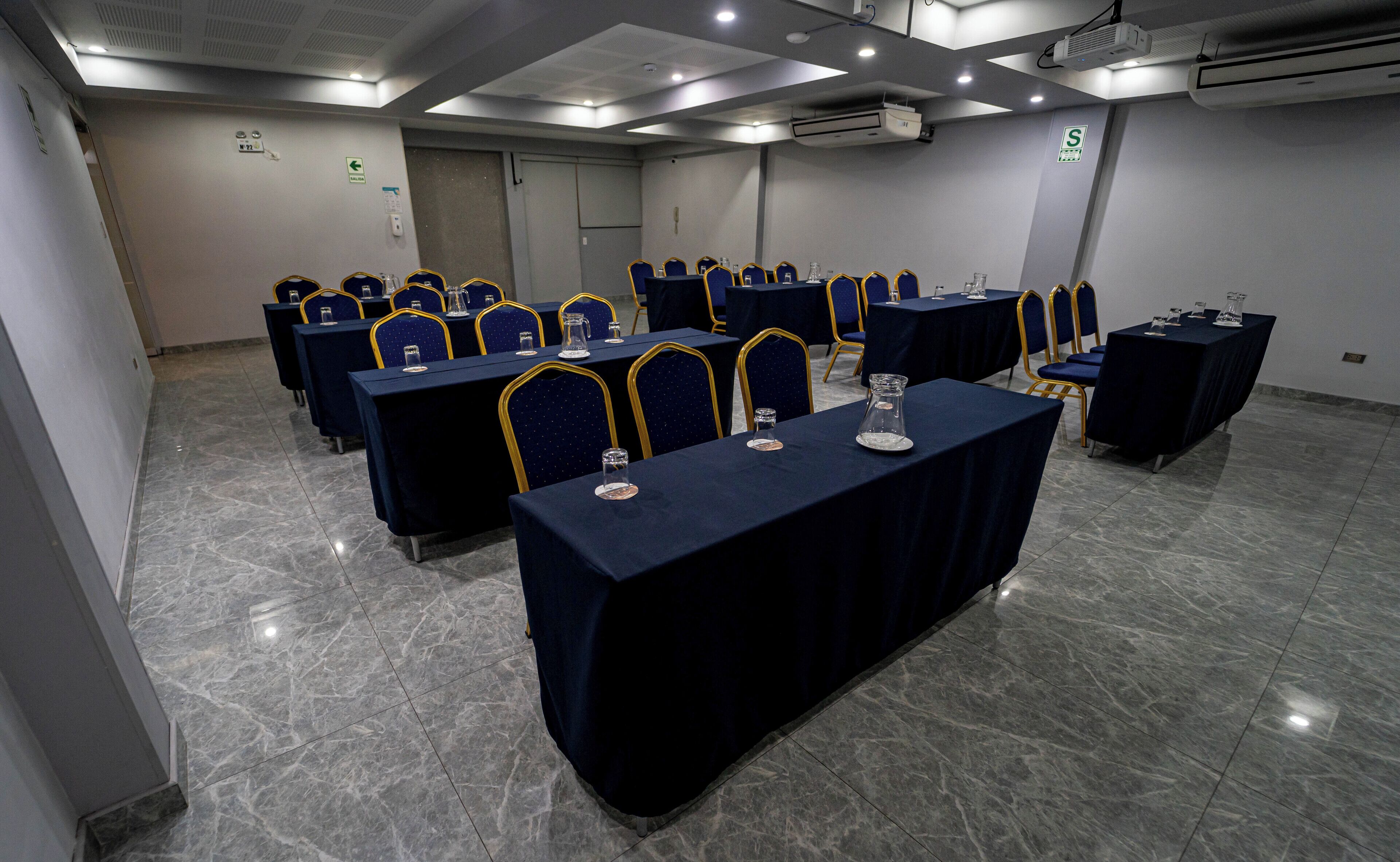 Un salón de conferencias con varias mesas y sillas, equipado con tarjetas de identificación y vasos de agua.
