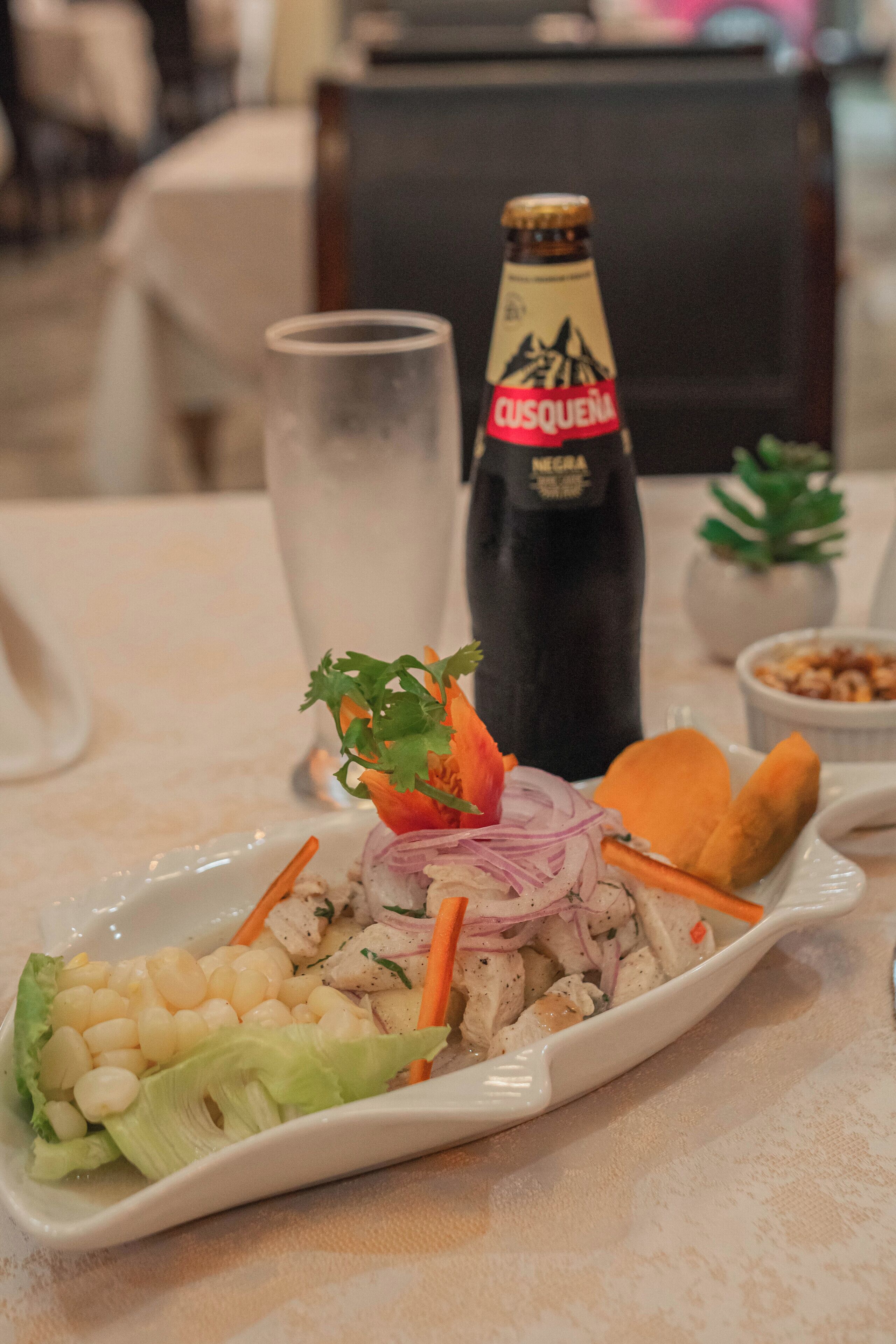 Una mesa de comedor con un plato de comida, una botella de cerveza y un vaso de agua.